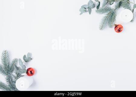Christmas composition with fir branches, eucalyptus foliage, candles and red ornaments on white background, flat lay. Stock Photo