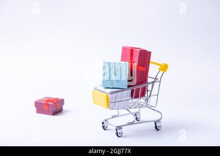 Miniature cart with gifts on a white background. Holidays shopping concept. Close-up. Stock Photo