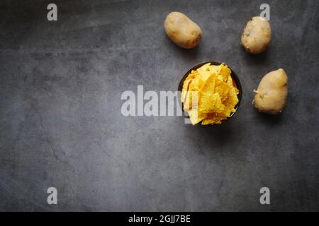 Bowl with tasty potato chips and potato on black background  Stock Photo