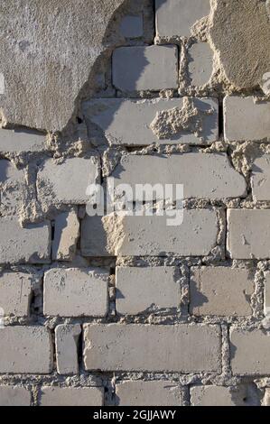 Painted in grey white colors old vintage empty brick wall background with Putty. Rustic cemented house stonewall texture with grunge surface. Shabby Building Facade With Damaged Plaster Stock Photo