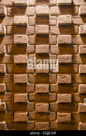 Red orange modern conceptual brick wall background with soft shadows illuminated from above at night. Shabby Building Facade With interesting pattern. House stonewall texture with copy space  Stock Photo