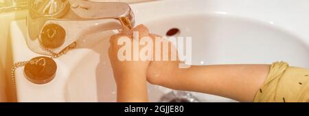 little kid washes his hands with run water under the faucet in a small sink at home in the bathroom. children clean and personal hygiene concept. peop Stock Photo