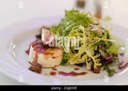 Hochzeitsträume - A gourmet salad served with baked goat cheese, fresh figs, and a drizzle of balsamic glaze on a white plate. Stock Photo