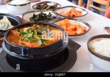 Korean signature Kimchi Stew in a hot ceramic pot served with other side dishes. Stock Photo