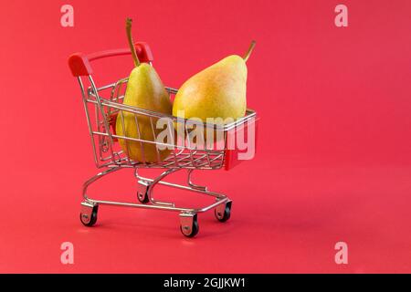 Close up view of little shopping cart withfresh juicy yellow pears on bright red background front view Stock Photo