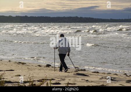 Old man doing cardio and muscular exercises outside. Active and healthy lifestyle. Nordic walking, training on a sandy beach sea shore in evening time Stock Photo