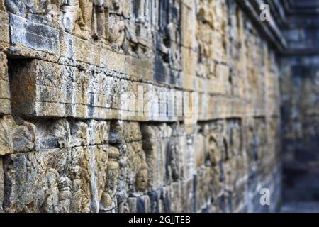 Interior of ancient Borobudur temple lower terraces. Close up of detail stone bas reliefs on the wall in corridor with bokeh background. No people. Stock Photo
