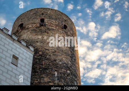 View up to an old brick fortified tower and house with white facade in front of blue sky with white clouds in evening light Stock Photo