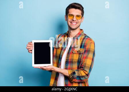 Portrait of attractive cheerful guy holding in hands device ebook copy space isolated over bright blue color background Stock Photo
