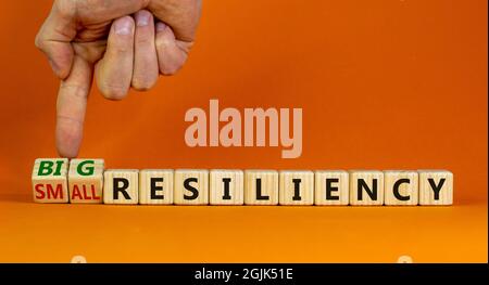 Big or small resiliency symbol. Businessman turns wooden cubes, changes words small resiliency to big resiliency. Beautiful orange background, copy sp Stock Photo