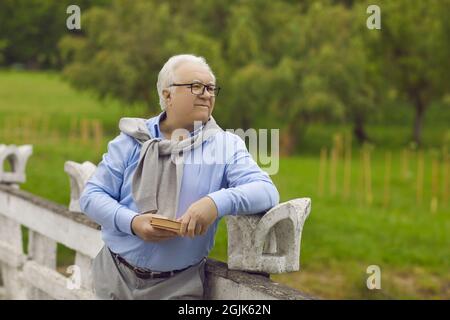 Happy elderly man with a book in his hands is resting in the park outdoors. Stock Photo