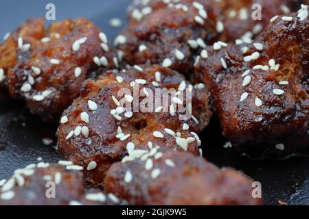 Sticky Asian cauliflower bites battered, deep-fried and tossed in Asian BBQ sauce, sprinkled with toasted sesame seeds and spring onion Stock Photo