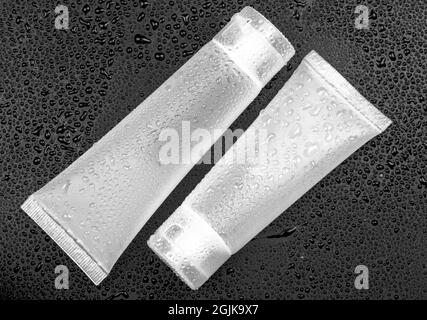 White tubes for cream on a black background with water drops Stock Photo