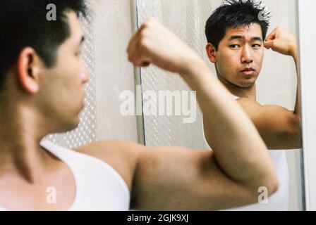 Mid 20's Asian man looking at himself in the bathroom mirror Stock Photo