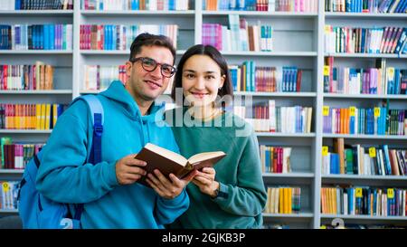 A young millennial student with glasses and a young attractive woman student are reading a book, preparing for an exam while standing in a public Stock Photo