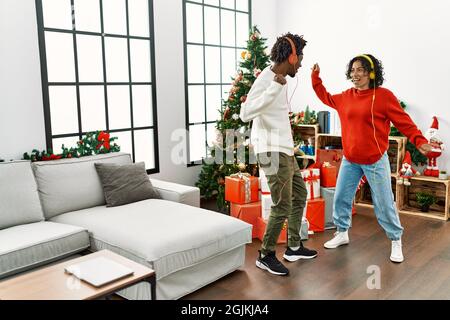 Young interracial couple smiling happy and and dancing standing by christmas tree at home. Stock Photo