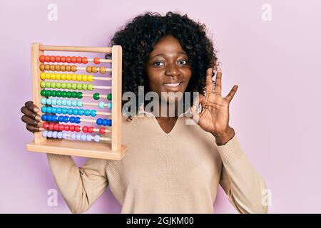 Young african american woman holding traditional abacus doing ok sign with fingers, smiling friendly gesturing excellent symbol Stock Photo