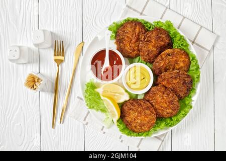 baked pork patties with cheese crust on a green lettuce lives with ketchup and mustard on a plate, flat lay Stock Photo