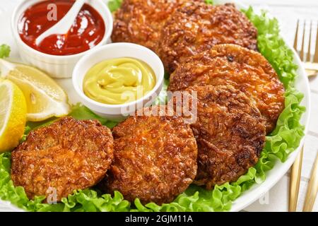 baked pork patties with cheese crust on a green lettuce lives with ketchup and mustard on a plate, close-up Stock Photo