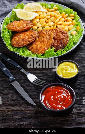 baked pork patties with browned cheese crust on a green lettuce lives with  lupine beans, ketchup and mustard on a plate Stock Photo