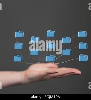 Vertical shot of computer file folders connected to the main cloud over a hand on a gray background Stock Photo