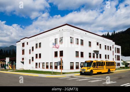 Skykomish, WA, USA - September 08, 2021; The K-12 rural school building in the Cascade Mountain town of Skykomish Washington with a yellow school bus Stock Photo