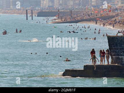 Crowded beaches of central Brighton and Hove. West of Brighton's Palace Pier. Summer holidays. Sussex, England, Kids jumping from the groynes. Stock Photo