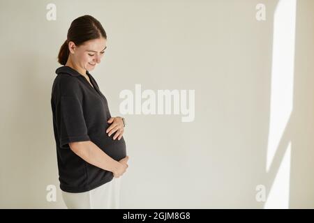 Happy beautiful pregnant young Caucasian woman with ponytail being in anticipation of baby embracing belly Stock Photo
