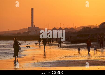 Brighton and Hove beach at low tide. Silhouettes of people walking along the sandy shore at sunset. East Sussex, England. Shoreham Power Station in the distance Stock Photo