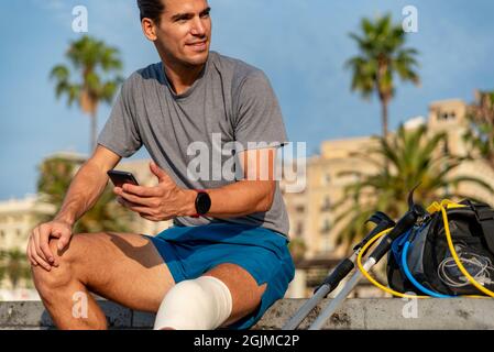 Young latin man with crutches using mobile phone after doing exercise Stock Photo