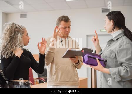 Two girls and a guy are talking in sign language. Three deaf students chatting in a university classroom. Stock Photo
