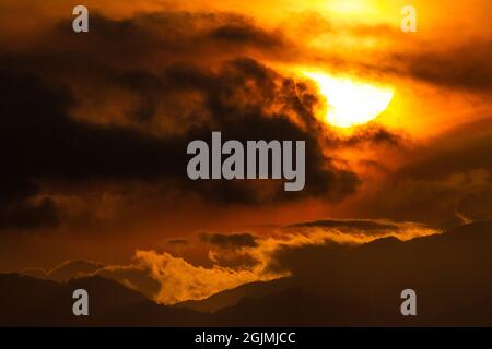 The disk of the sun at sunset in dramatic clouds over mountains in  Japan. Stock Photo