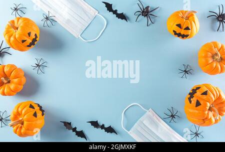 Halloween decorations made from pumpkin, paper bats and surgical face mask on pastel blue background. Flat lay, top view of Halloween celebration duri Stock Photo