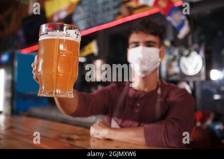 Selective focus on beer mug in the hand of male brewer, wearing medical face mask Stock Photo
