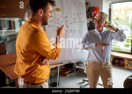 A senior business woman has a conversation with her male colleague while holding a presentation in a pleasant atmosphere at workplace. Business, offic Stock Photo