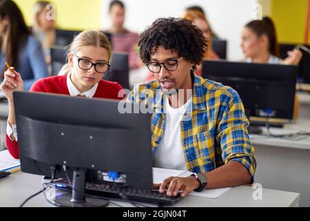 Students at the informatics lecture working together in the university computer classroom. Smart young people study at the college. Education, college Stock Photo