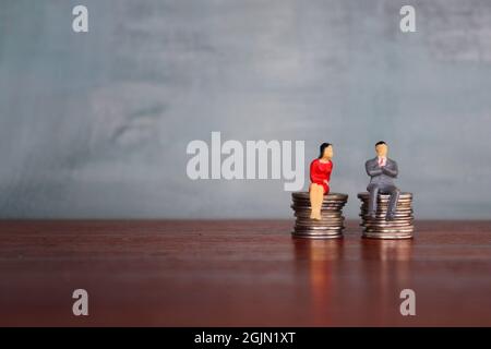 Concept of equal pay, Miniature man and woman sitting on a stack of coins with the same height. Copy space for text Stock Photo