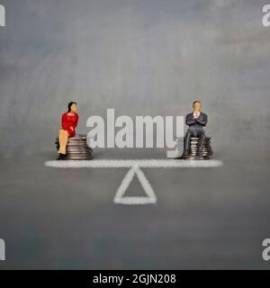 Gender equality and equal pay concept. A miniature man and woman sit on a stack of coins and balance scale. Stock Photo