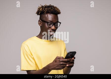 Serious focused African American man in glasses using cellphone, surfing internet, customer shopping online, browsing mobile device apps, holding smar Stock Photo