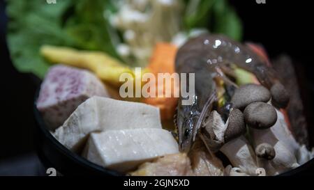 Spicy Chinese hot pot with fresh raw seafood, tofu, prawns, mushrooms, green leaves for lunch at restaurant. Delicious food for cooking Taiwanese hotp Stock Photo