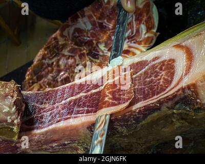 A front leg of Serrano Iberian ham also known as Spanish Pata Negra mounted  on a wooden stand with a butcher cutting slices Stock Photo - Alamy