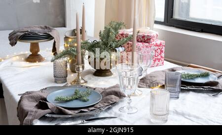Christmas table setting for a festive dinner. Dinnerware, candles and gift boxes on the set table in honor of Christmas. An elegantly set table for ce Stock Photo