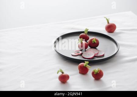Fresh red radishes with stem and roots in a black dish on table