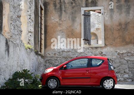 Sparkling red Citroen car parked front of an abandoned house in Galaxidi, Phocis Greece. Stock Photo