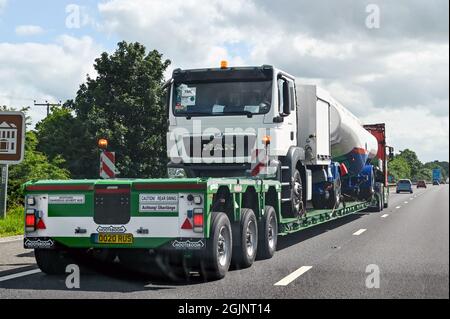 Swindon, England - June 2021: Low loader articulated lorry loaded with a heavy tanker vehicle load on the M4 motorway. Stock Photo