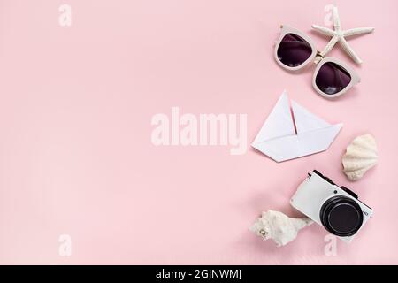 Photo camera, white sunglasses, origami boat, seashells and starfish on pink background, top view with copy space Stock Photo
