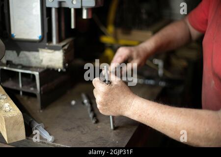 A man pulls out a drill. Installing a drill for a drill. Works in the garage. The master's hands hold the part of the electrical equipment for drillin Stock Photo