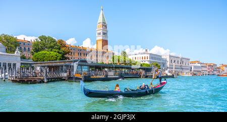 VENICE, ITALY - AUGUST 02, 2021: Tourists on gondola and Venice cityscape with St Mark Campanile, Italian: Campanile di San Marco, on background. Venice, Italy. Stock Photo