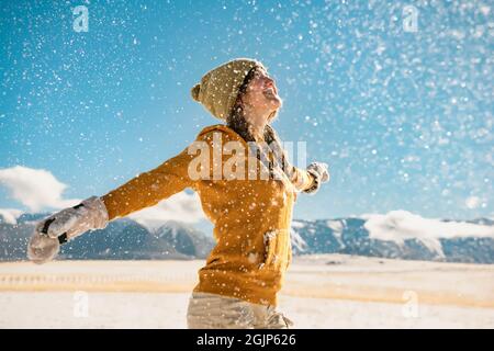 Young happy stylish girl whirls with raised hands and enjoys the snow in mountains. Winter holidays concept Stock Photo