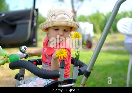 Close-up of a little girl in a summer hat. Portrait of a cute little girl in a hat look down sitting on a small bicycle Stock Photo